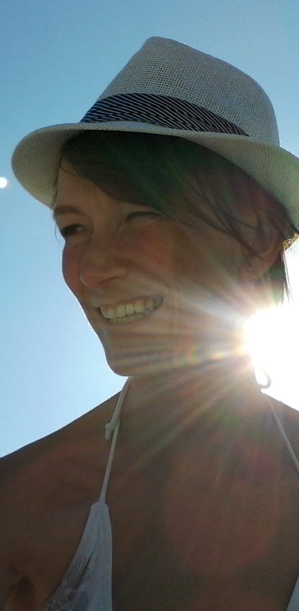 Junge Frau mit Sonnenhut lächelt vor hellem, sonnigem Hintergrund.